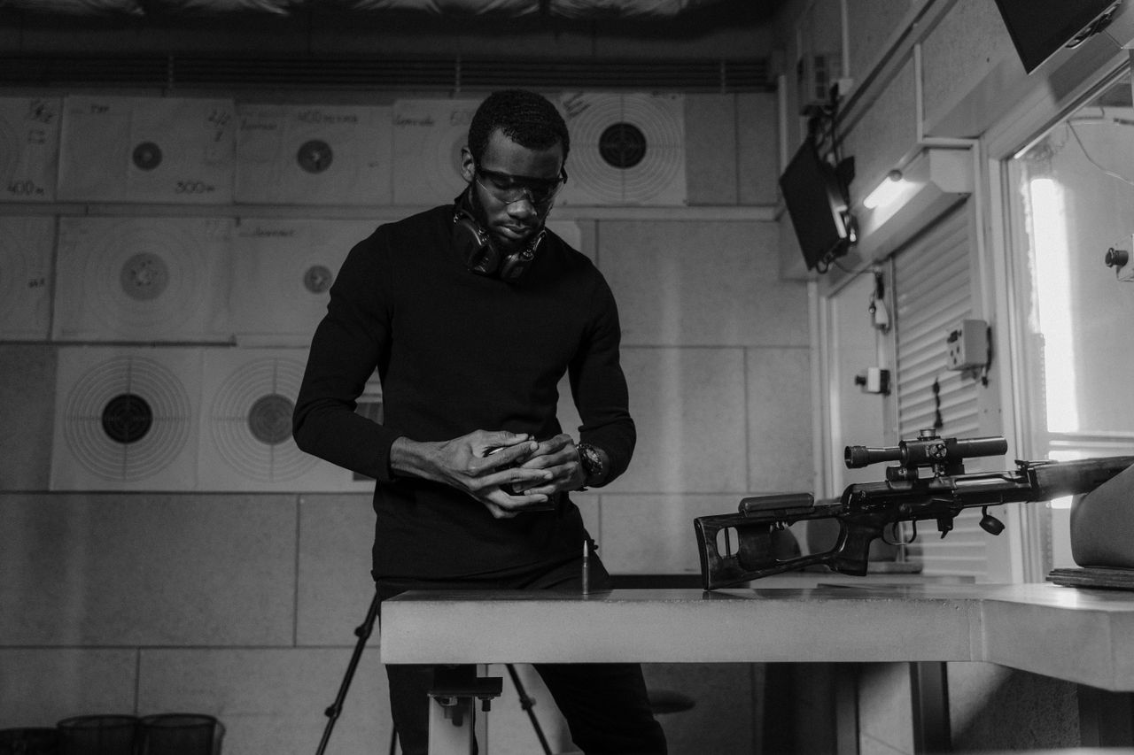 Services Black and white photo of a man handling a firearm at an indoor shooting range.