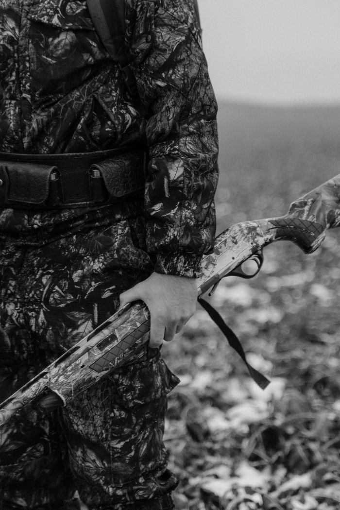 About A hunter in camouflage holding a rifle outdoors, captured in monochrome.