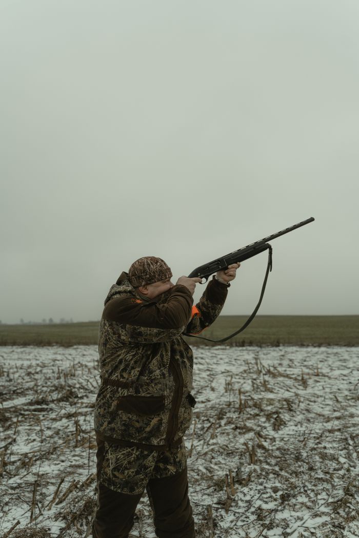 Services Hunter in camouflage aiming a rifle in snowy field.